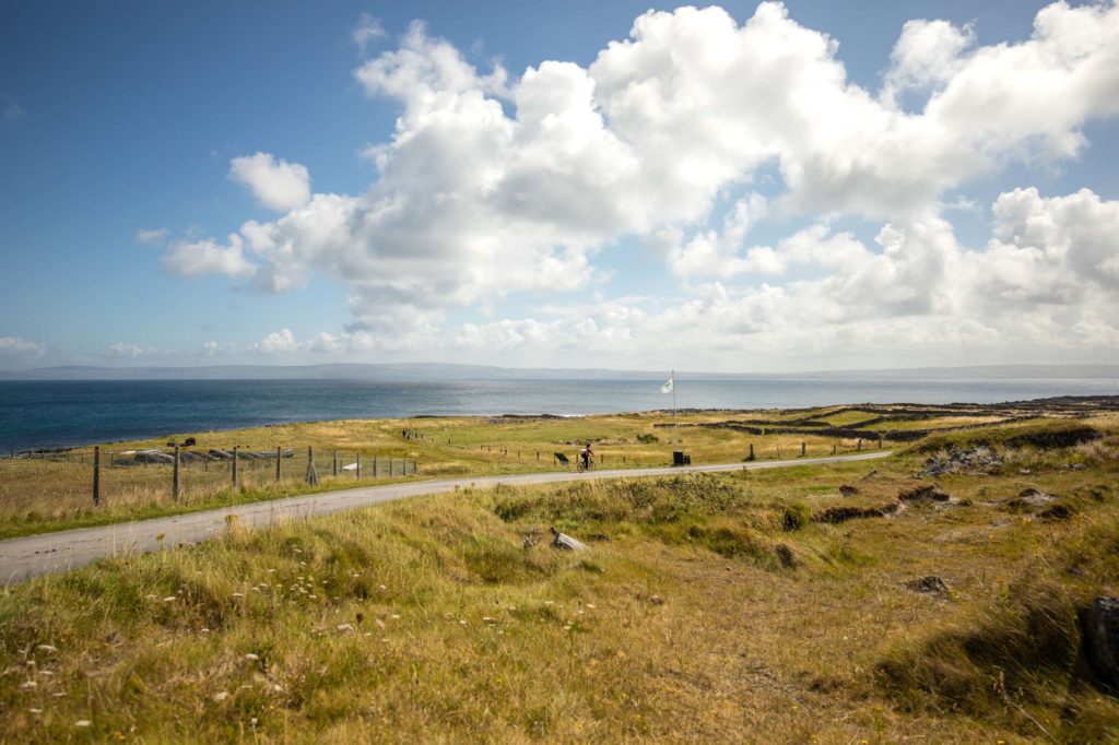 AKphoto (105) Scenic coastal landscape with grassy fields, a winding path, and bright clouds, possibly in Ireland or the UK.