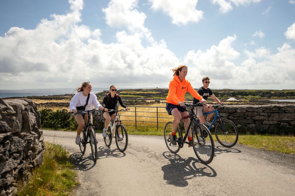 AKphoto (110) Group cycling along scenic Irish countryside with stone walls and lush fields under a partly cloudy sky.
