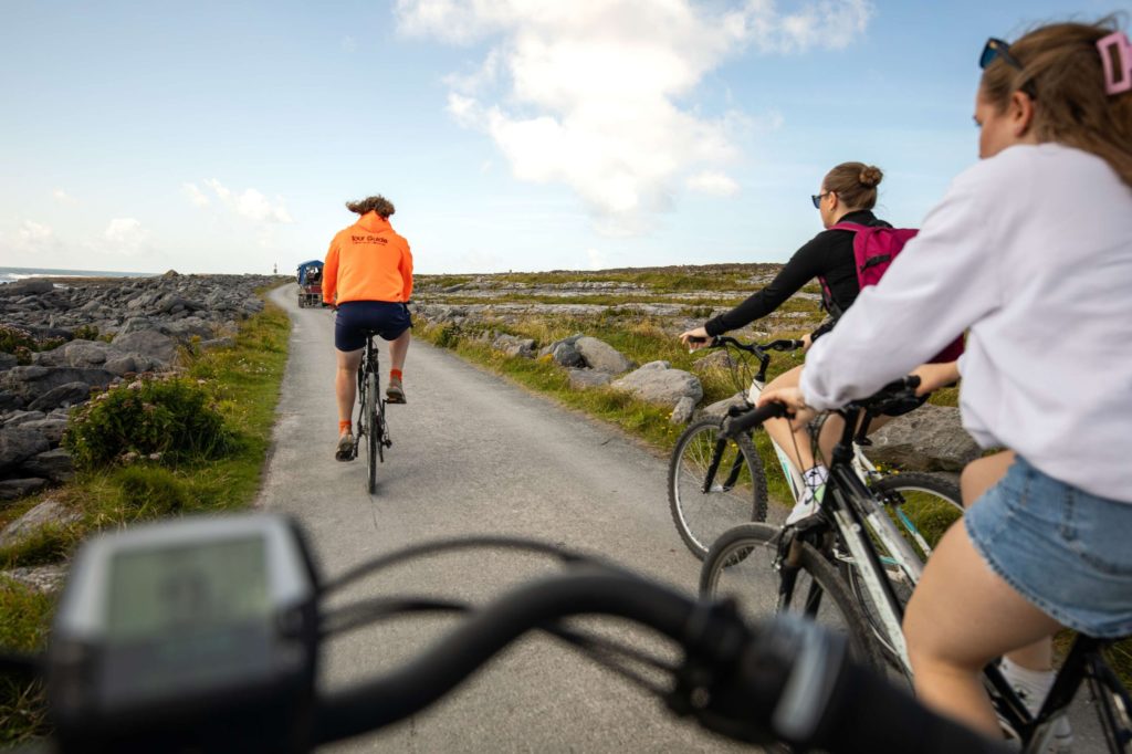 AKphoto (126) Cyclists enjoy a scenic ride along a coastal path, led by a guide in an orange jacket, under a clear blue sky.