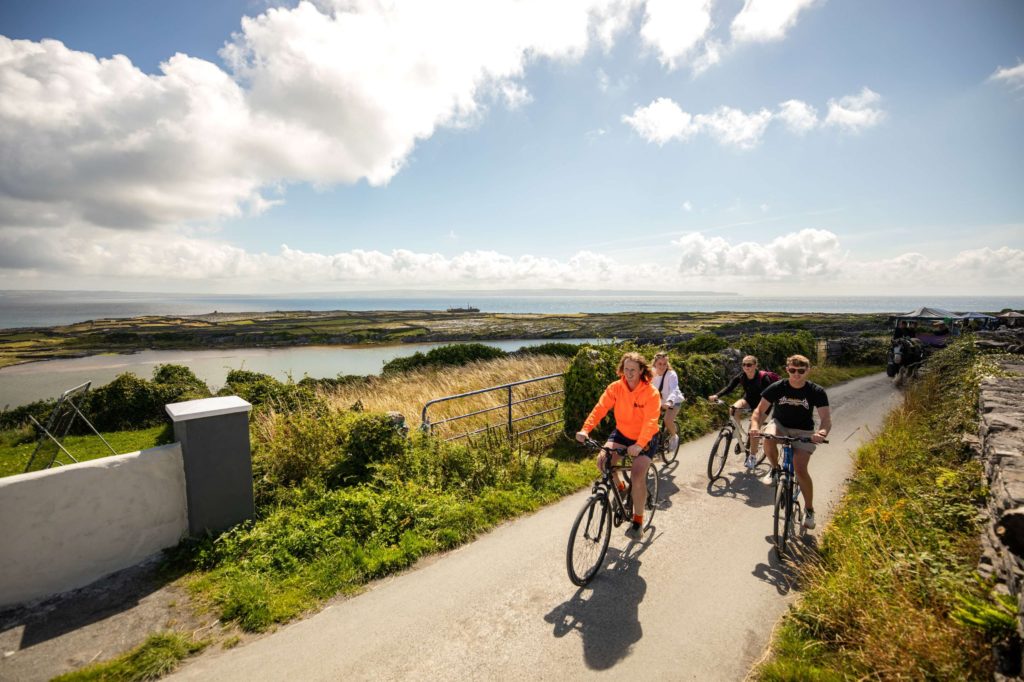 AKphoto (131) Cyclists enjoying a scenic coastal ride on a sunny day, with lush greenery and the ocean in the background.