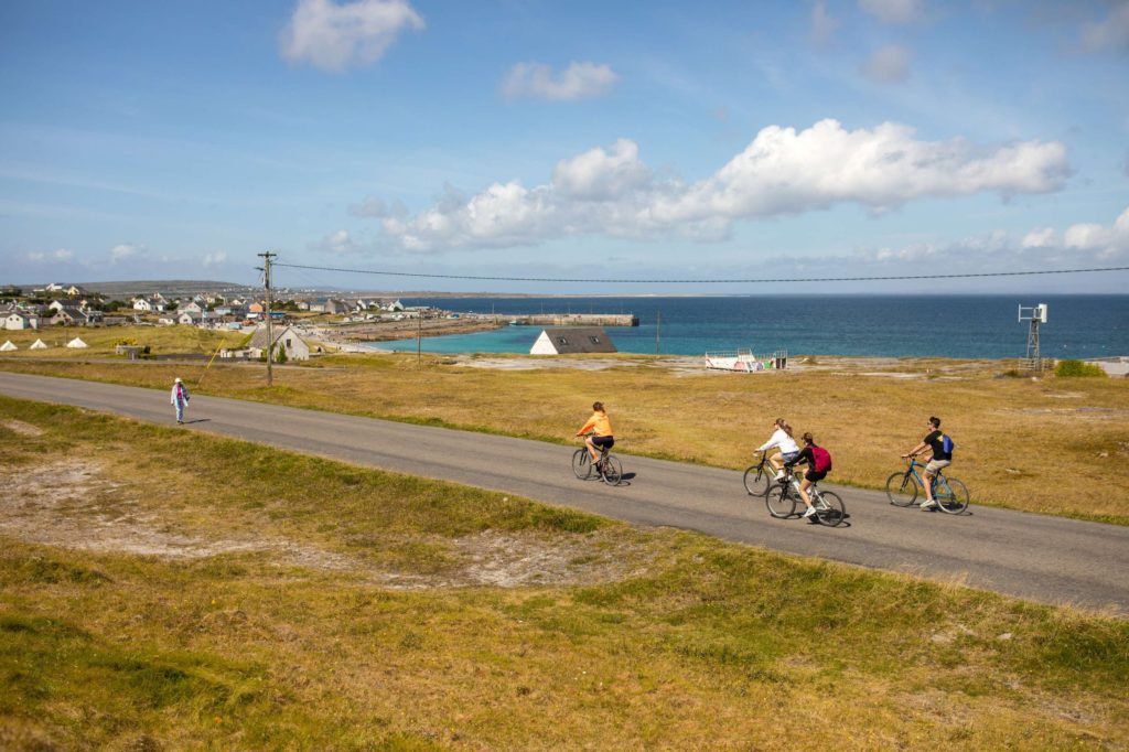 AKphoto (140) Cyclists enjoy a scenic ride on an Irish coastal road, with small houses and blue ocean in the background.