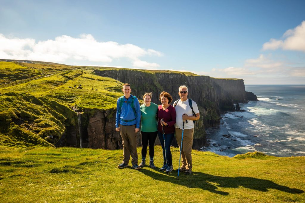 AKphoto (151) Group of hikers enjoying a sunny day at the Cliffs of Moher, Ireland, with stunning ocean and landscape views.