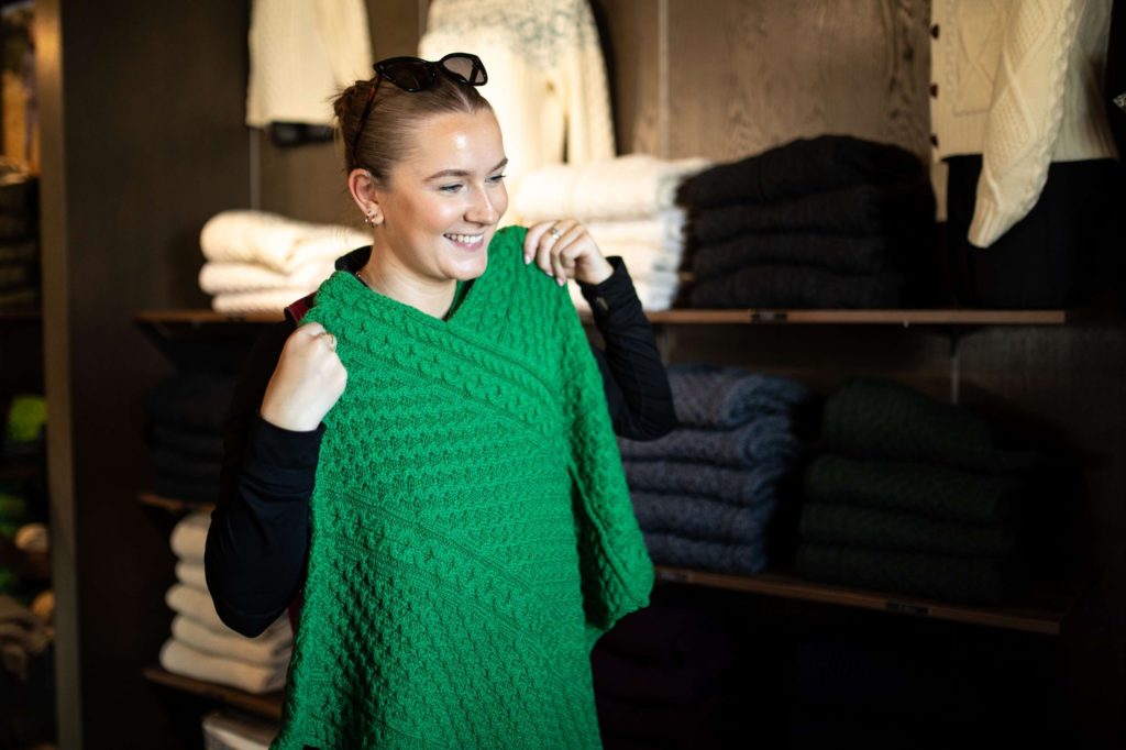 AKphoto (151) Woman smiling while trying on a vibrant green knit sweater in a cosy clothing shop.