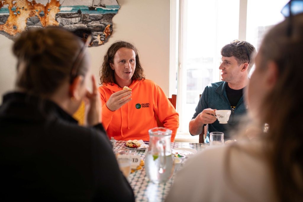 AKphoto (16) Group enjoying a discussion over tea at a table with pastries and beverages in a cosy dining room setting.