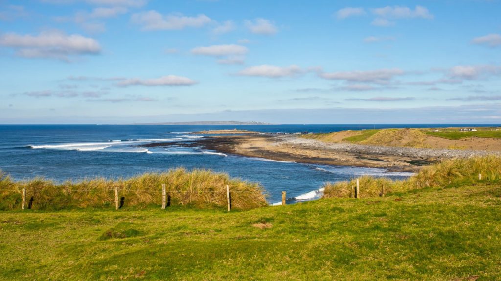 AKphoto (17) Coastal landscape with grassy cliffs and blue ocean waves under a sunny sky.