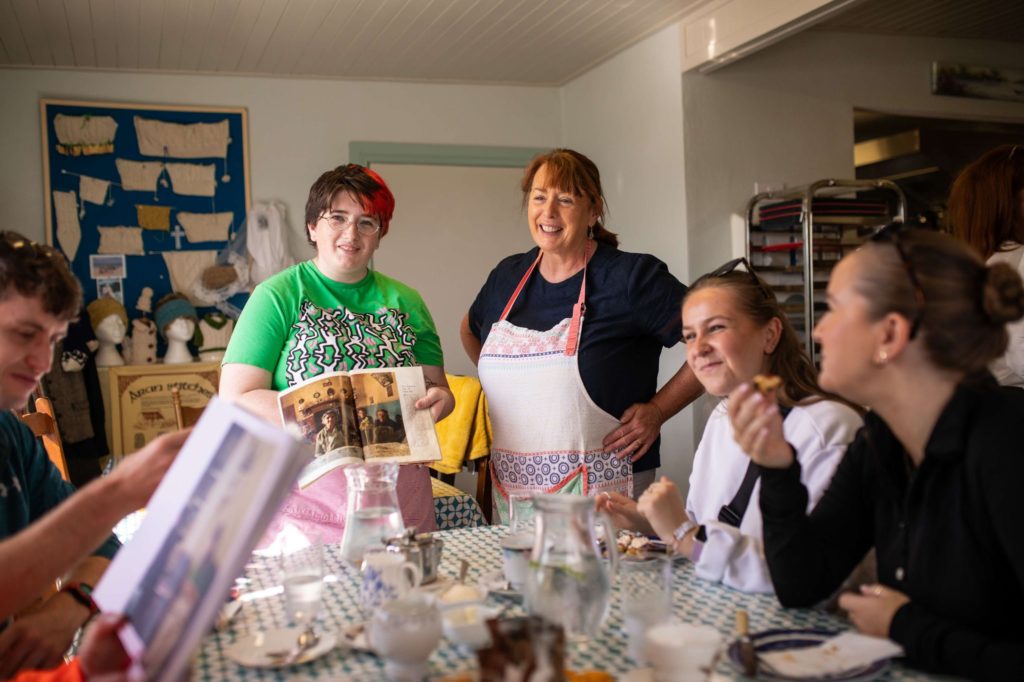 AKphoto (20) Group enjoying a cosy knitting workshop with tea and books at a table in a welcoming community setting.