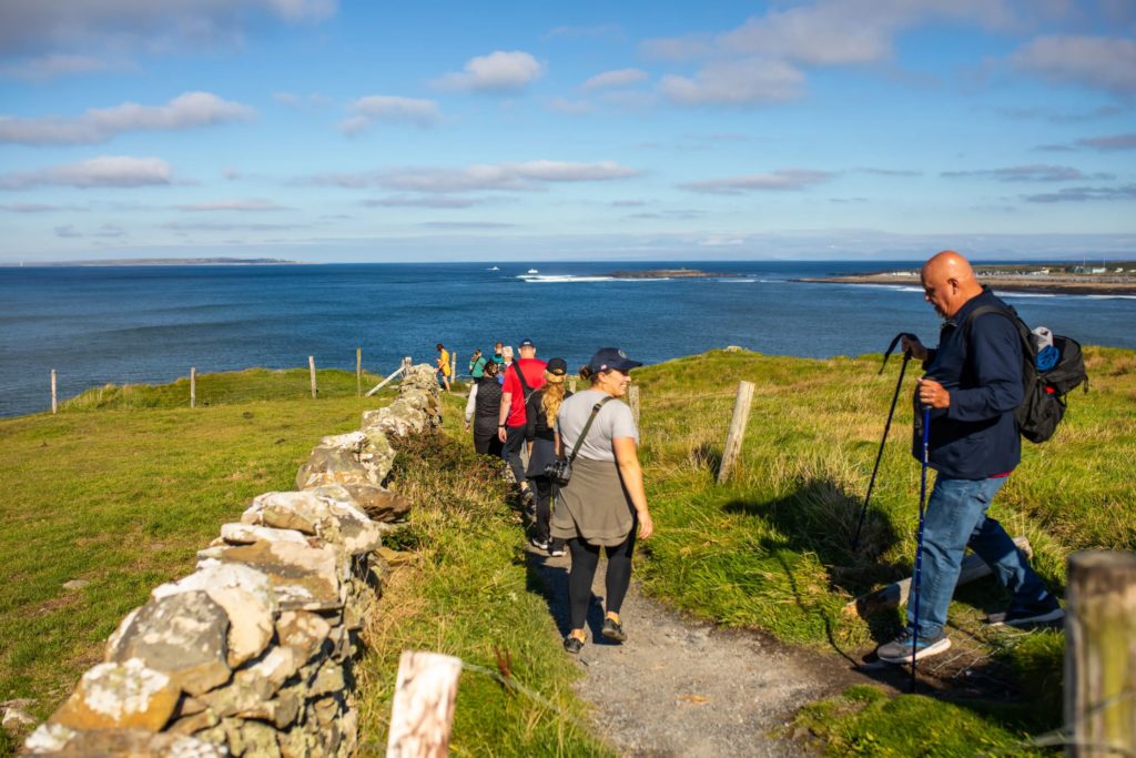 AKphoto (24) Hikers walk along a scenic coastal trail with ocean views under a clear sky.