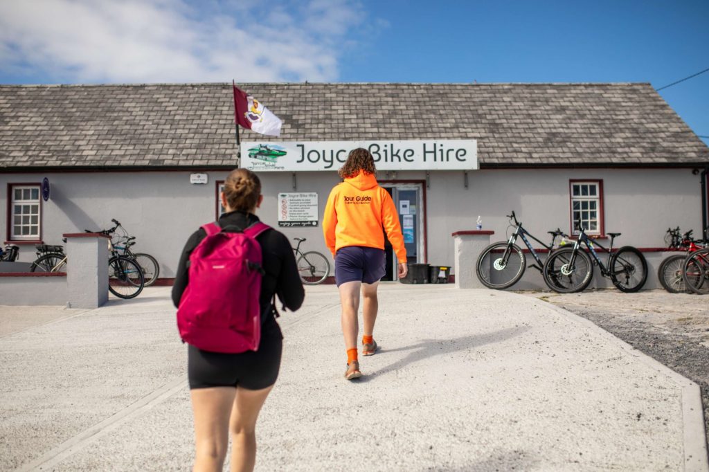 AKphoto (28) People approaching Joyce Bike Hire shop with bicycles in the foreground on a sunny day.
