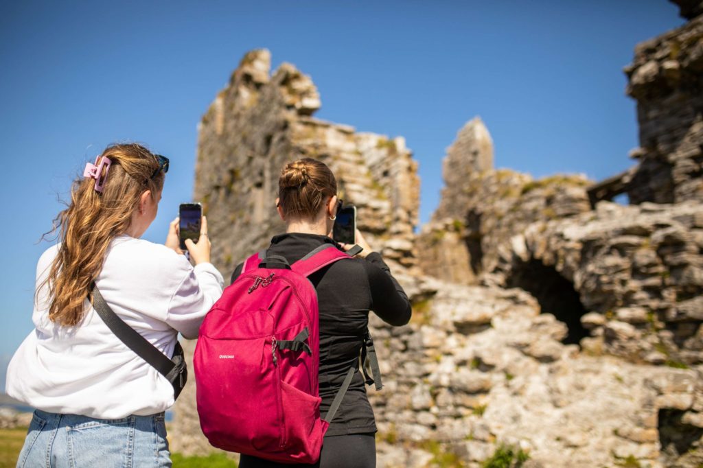 AKphoto (51) Two tourists photographing ancient stone ruins under a clear blue sky in Ireland.