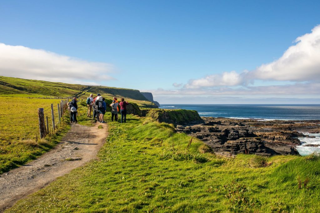 AKphoto (59) Group hiking along scenic coastal cliffs with blue skies and ocean views.