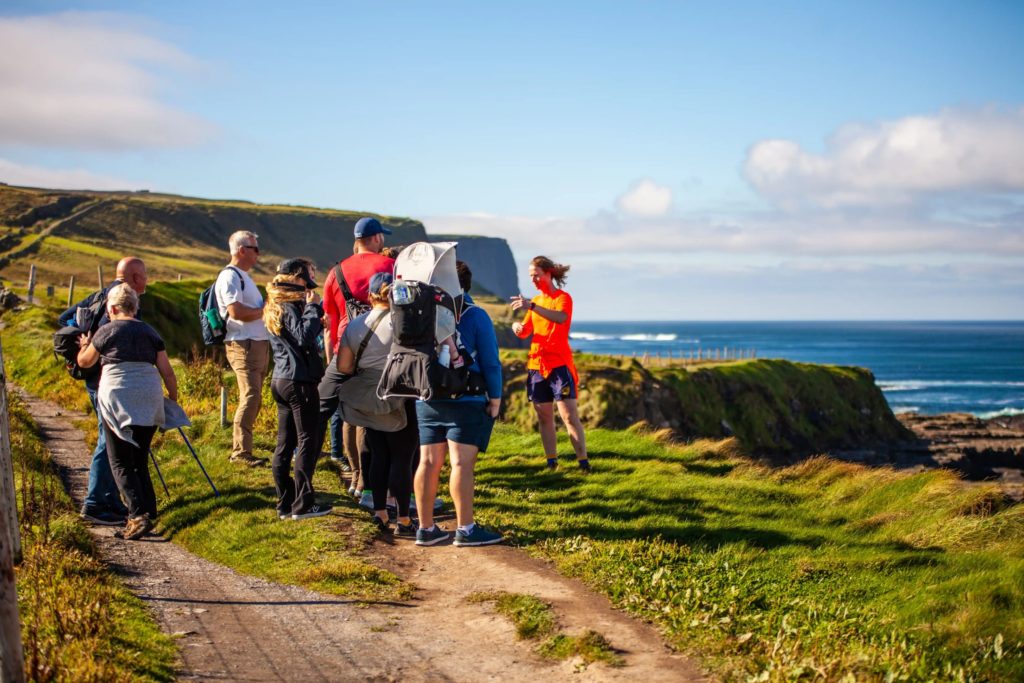 AKphoto (63) Group of hikers listening to a guide along coastal cliffs with a blue ocean backdrop under a clear sky.
