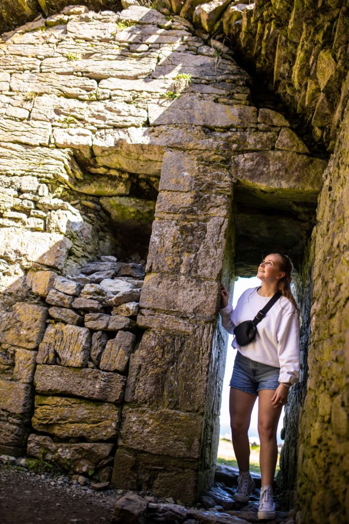 AKphoto (66) Young woman explores ancient stone ruins, wearing casual attire, in bright sunlight.