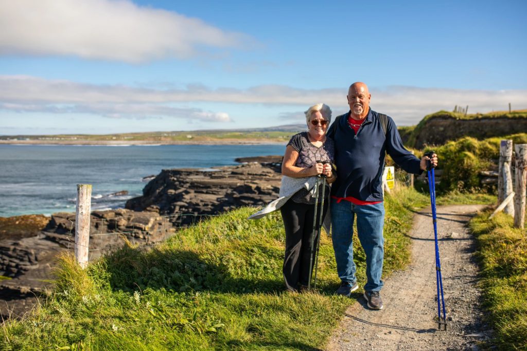 AKphoto (81) Elderly couple hiking along coastal path in Ireland, enjoying the scenic sea view on a sunny day.