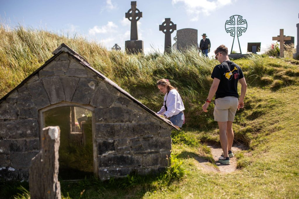 AKphoto (85) Two people exploring an ancient Irish graveyard with Celtic crosses under a clear blue sky.