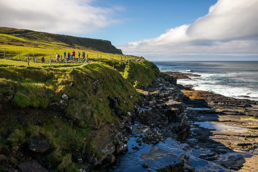 AKphoto (92) Group of hikers enjoying the scenic cliffs and ocean views along Ireland's rugged coastal trail under a sunny sky.