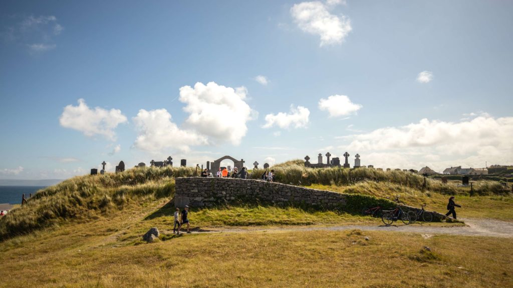 AKphoto (92) Historic seaside graveyard with Celtic crosses on a sunny hill, cyclists and visitors enjoy the scenic landscape.